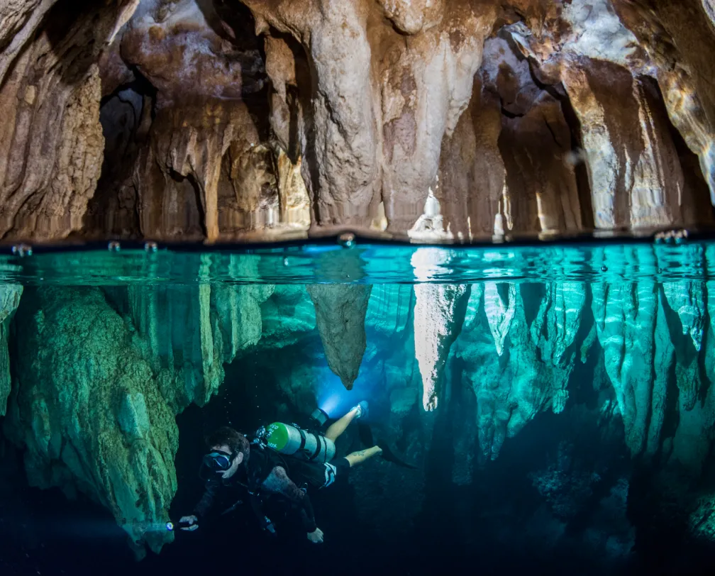 scuba diver in clear water in Chandelier Cave in Palau with stalactite and stalactites above and beyond