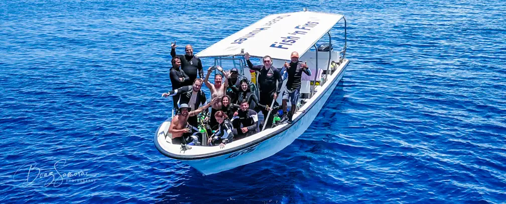 front shot of a dive boat from Fish 'n Fins with divers waving at the camera
