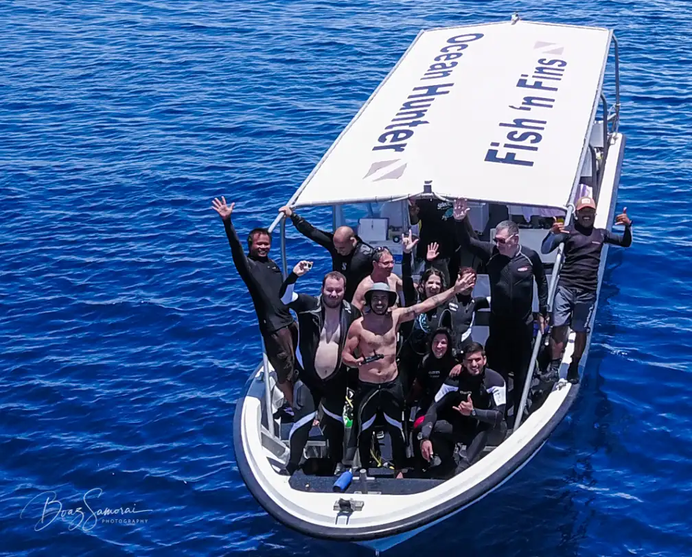 divers on a fish 'n fins boat waving at a drone which takes a picture of the boat from about 30 degrees down